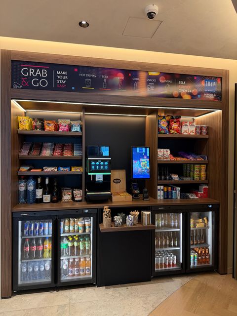 Snack- en drankbalie van een gemakswinkel met verlichte koelkasten en schappen vol snoep en chips.