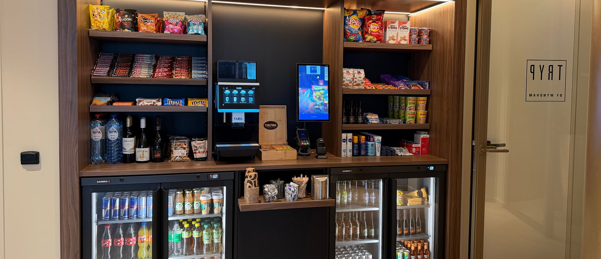 Snack- en drankpresentatie in een gemakswinkel met een digitale kiosk en koelkasten met glazen deuren.