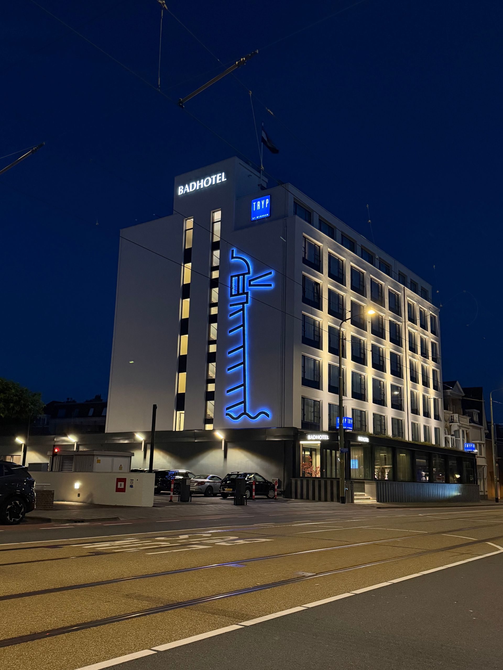 Modern wit kantoorgebouw van meerdere verdiepingen met grote ramen aan een stadsstraat onder een blauwe hemel.