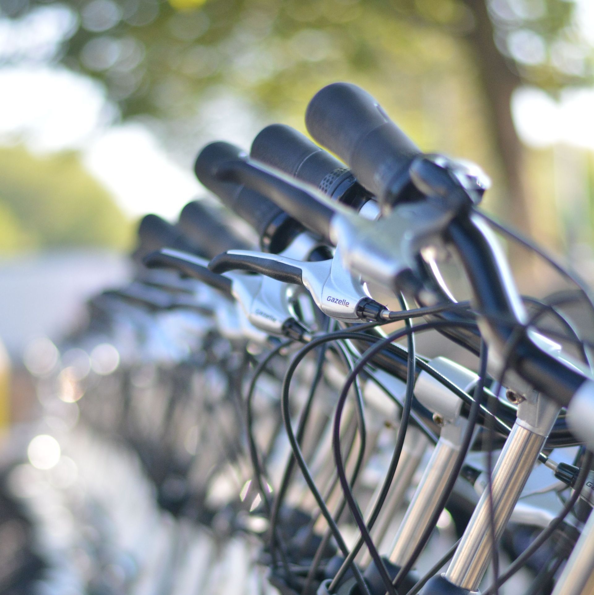 Een rij geparkeerde fietsen met de sturen scherp in beeld, buiten op een zonnige dag.