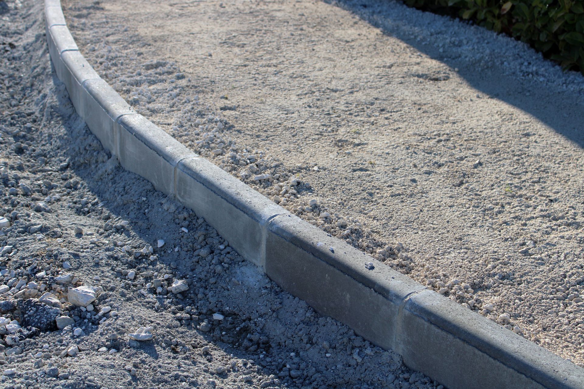 Bordure en béton incurvée délimitant un chemin de gravier.
