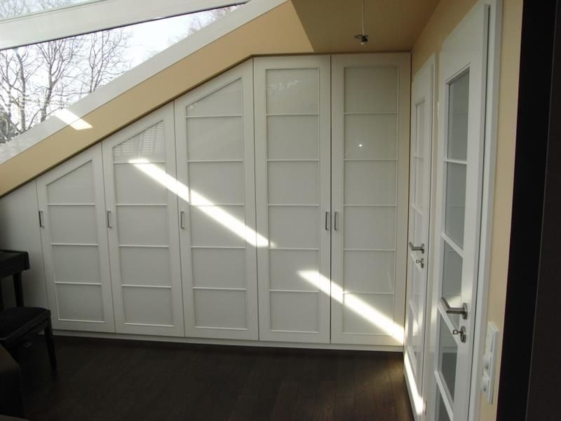 Ein Raum mit Dachschräge und weißen Schränken