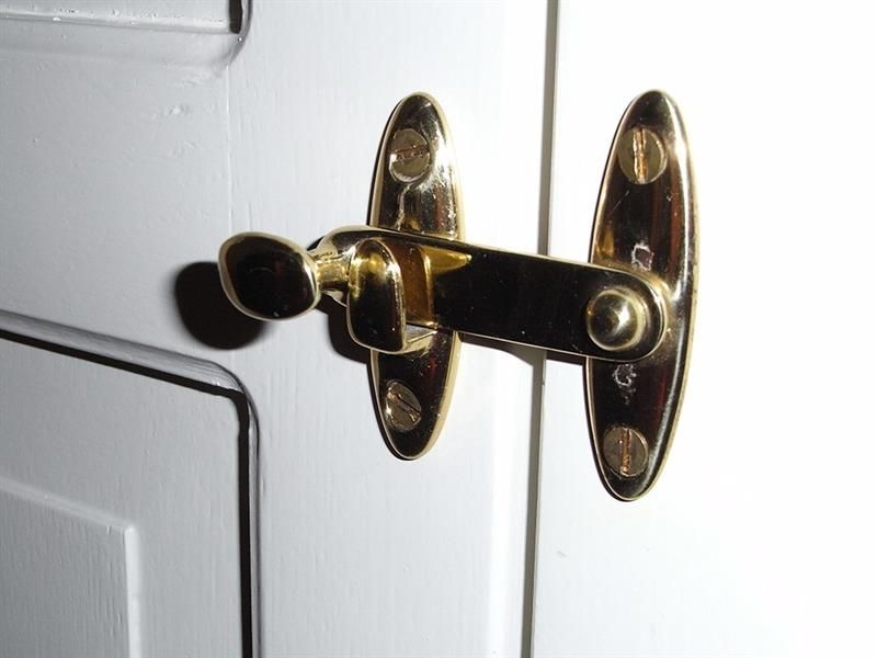 An einer weißen Tür ist ein Messingtürriegel befestigt