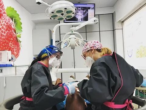 Dos dentistas están trabajando con un paciente en un consultorio dental.