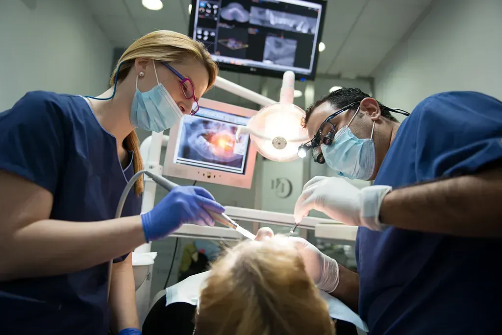 Una mujer se está haciendo examinar los dientes por dos dentistas