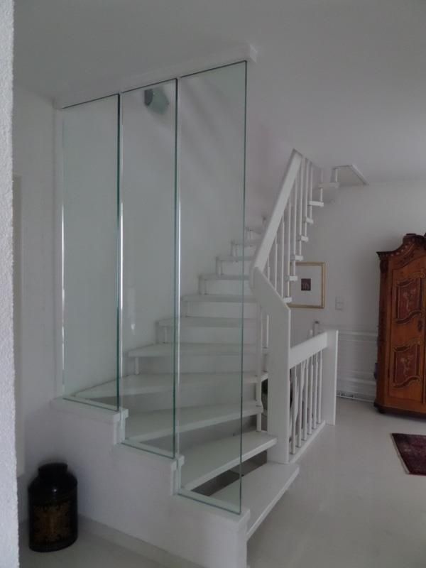 Eine weiße Treppe mit Glasgeländer in einem Wohnzimmer