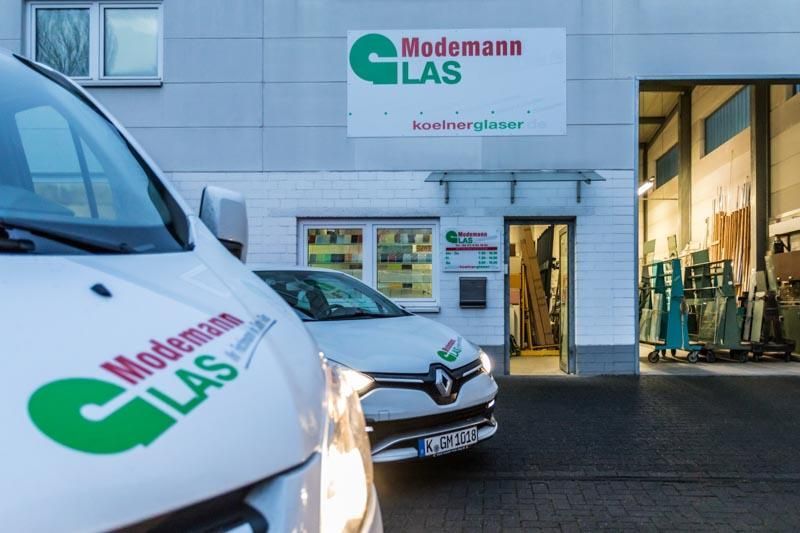 Zwei weiße Lieferwagen stehen vor einem Gebäude mit der Aufschrift „Modemann Glas“