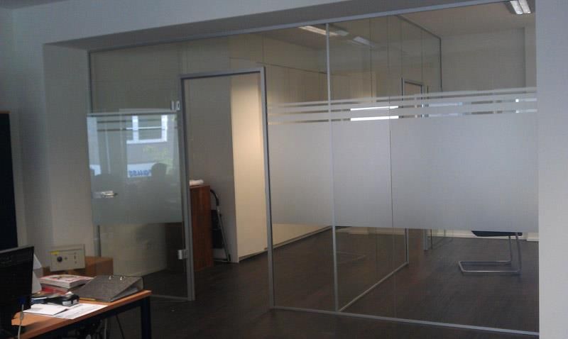 Ein Raum mit einer Glaswand und einem Schreibtisch mit einem Laptop darauf.