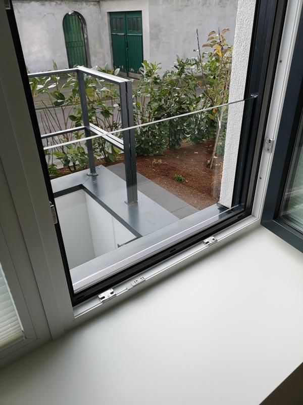 Ein Fenster mit Blick auf einen Garten und einen Balkon.