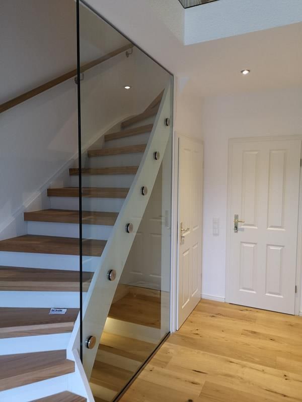 Eine Treppe mit einem Glasgeländer und Holzstufen in einem Flur.