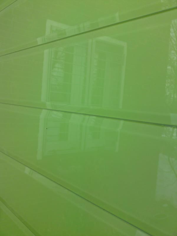 Eine Nahaufnahme einer grünen Wand mit der Spiegelung eines Gebäudes darin.