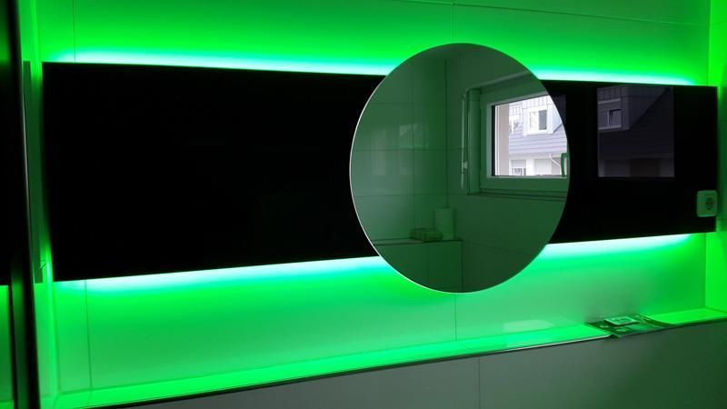 Vor einer grün beleuchteten Wand steht ein Spiegel.