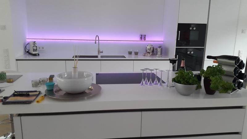 Eine Küche mit weißen Schränken und einer violetten Lampe an der Wand.