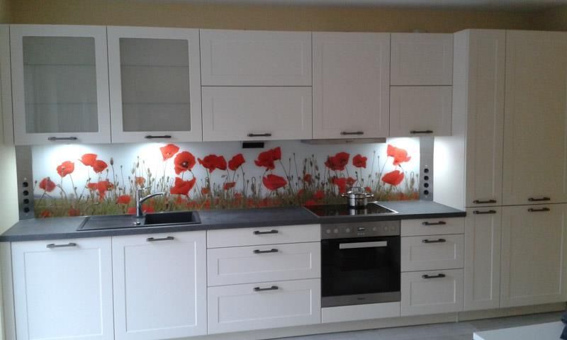 Eine Küche mit weißen Schränken und roten Blumen an der Rückwand