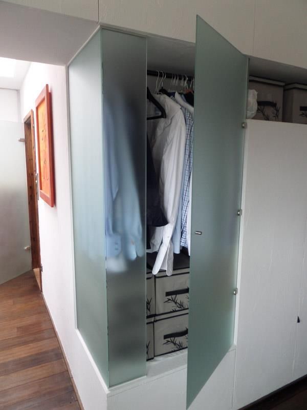 Ein Schrank mit einer Milchglastür und Kleidung darin