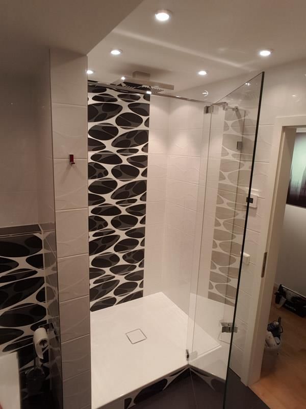 Ein Badezimmer mit ebenerdiger Dusche und einer schwarz-weiß gefliesten Wand.