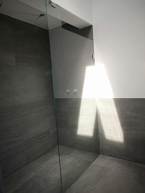 Ein Badezimmer mit ebenerdiger Dusche und Glastür.