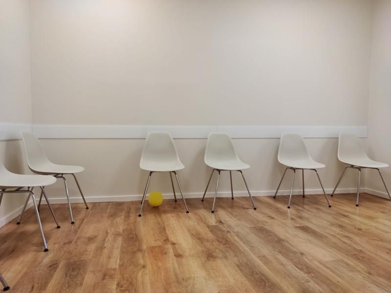 Eine Stuhlreihe in einem Wartezimmer mit einem gelben Ball in der Mitte.