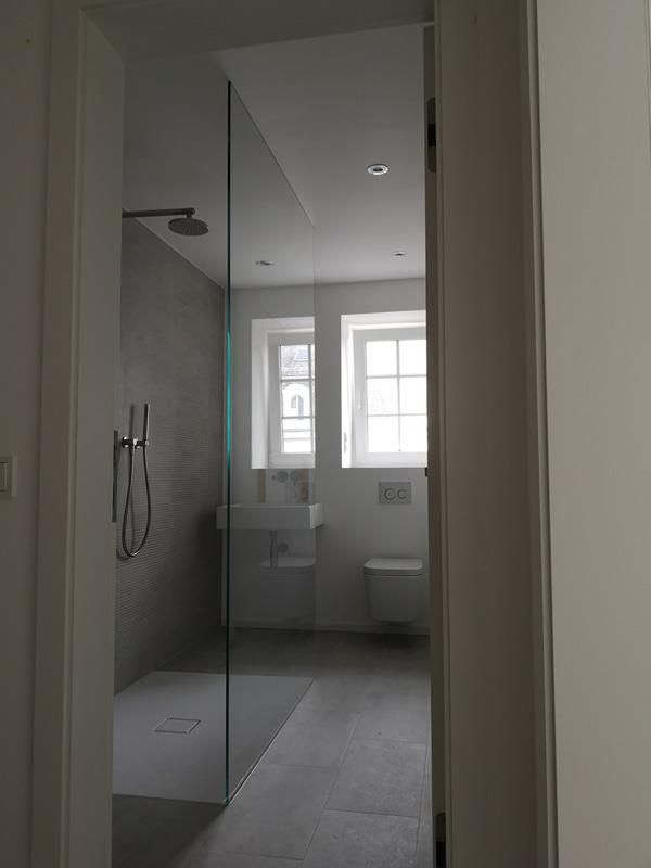 Ein Badezimmer mit ebenerdiger Dusche, Waschbecken, Toilette und Fenster.