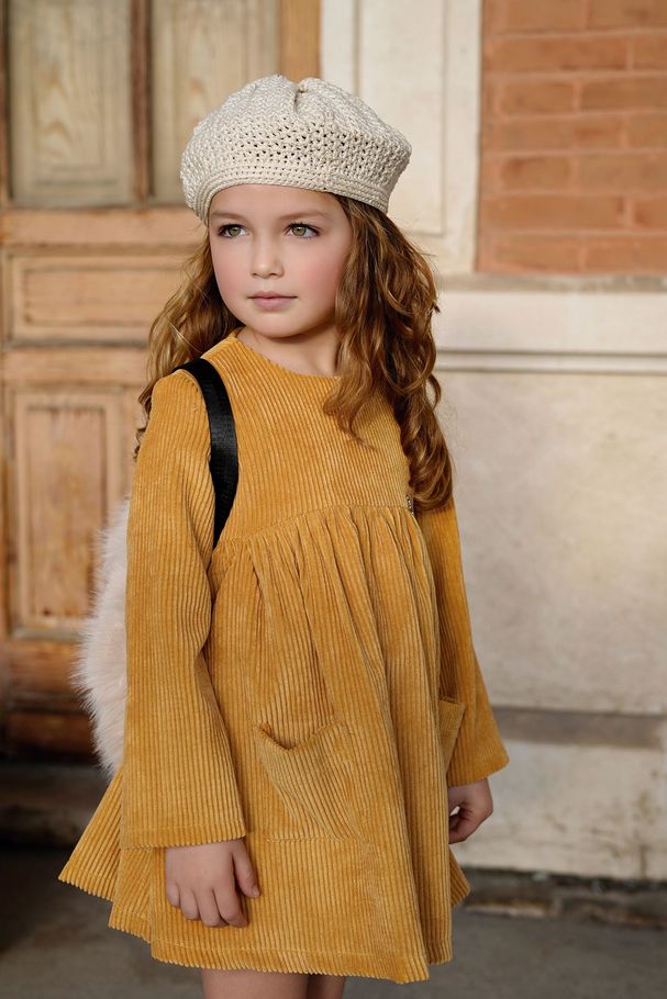 Una niña con un vestido y zapatillas deportivas está de pie junto a un pilar.