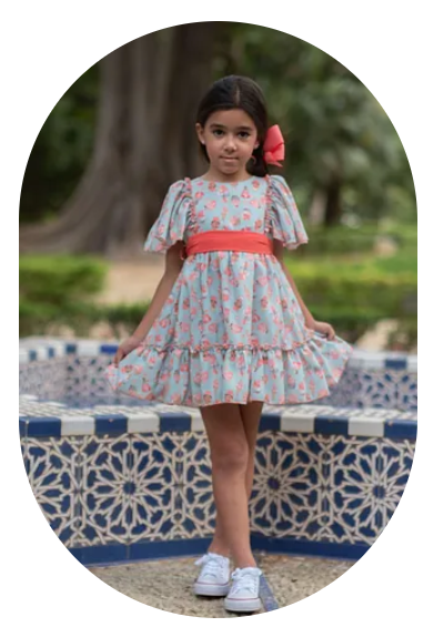 Una niña con un vestido está parada al lado de un banco.