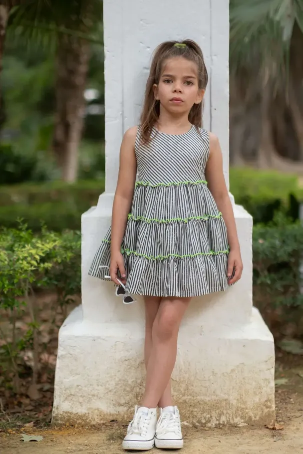 Una niña con un vestido y zapatillas deportivas está de pie junto a un pilar.
