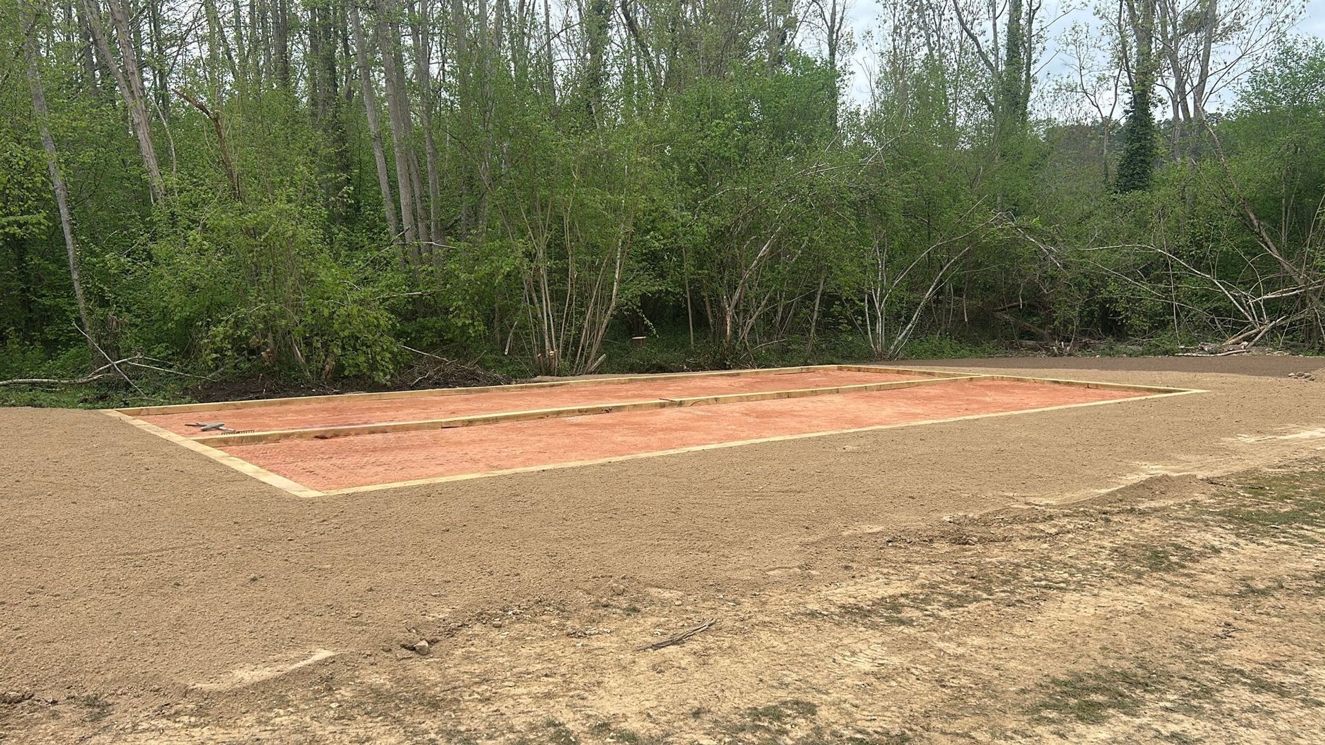 Terrain de sable extérieur avec bordure blanche, bords herbeux et arbres sous un ciel nuageux.
