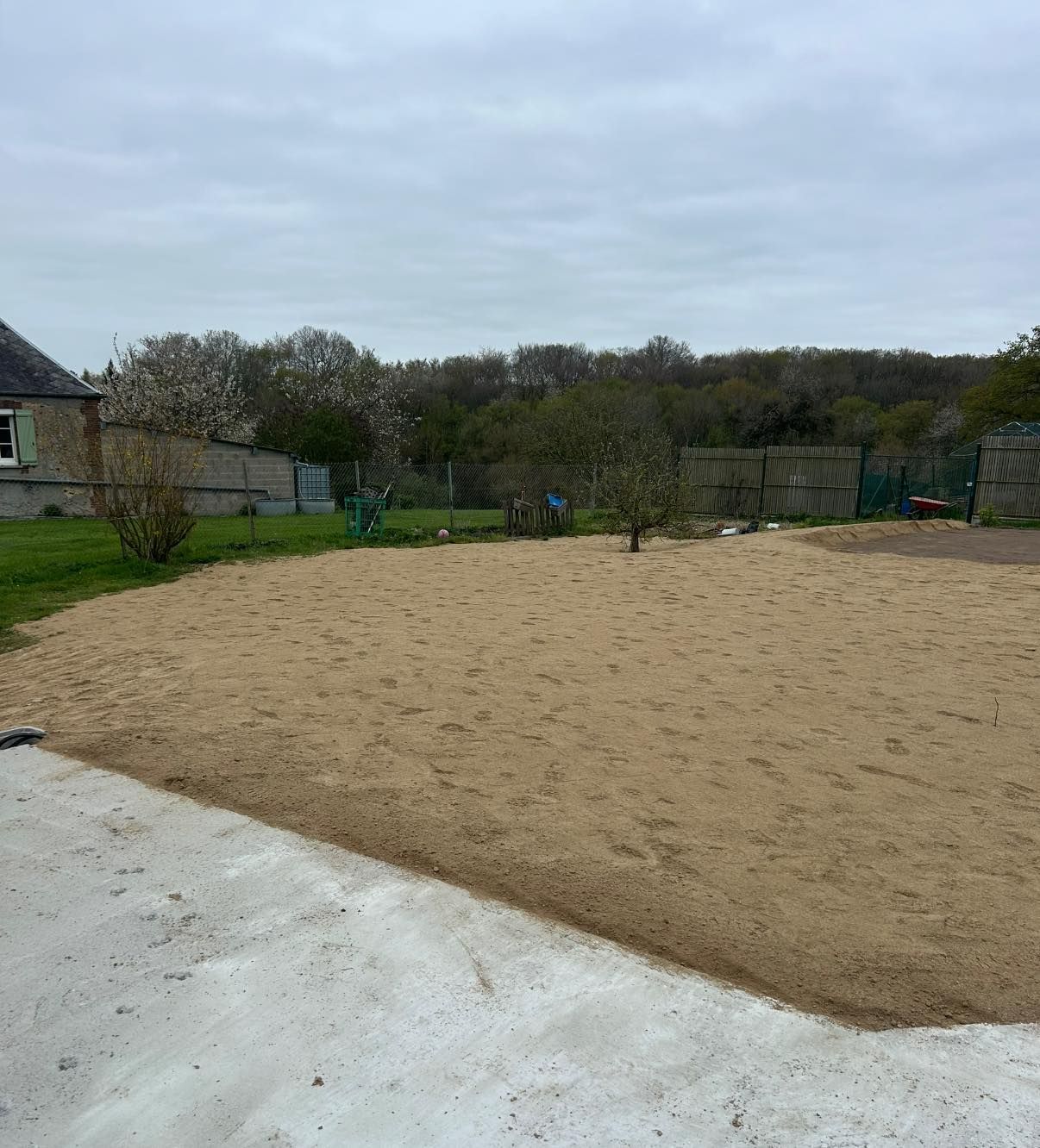 Terrain de sable extérieur avec bordure blanche, bords herbeux et arbres.