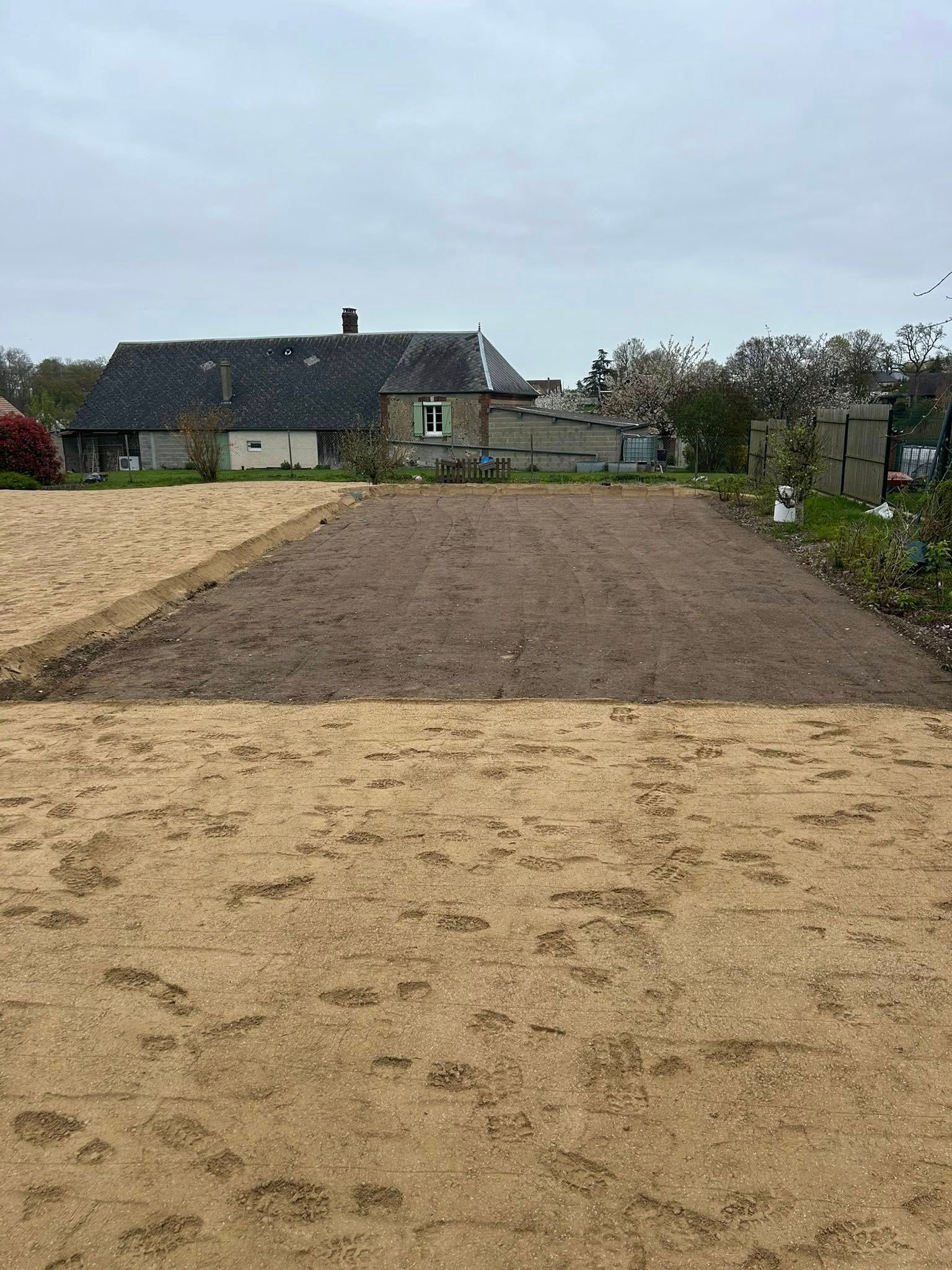 Parcelle de jardin fraîchement labourée devant une maison sous un ciel nuageux.