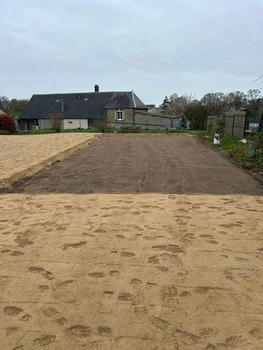 Parcelle de jardin fraîchement labourée devant une maison sous un ciel nuageux.