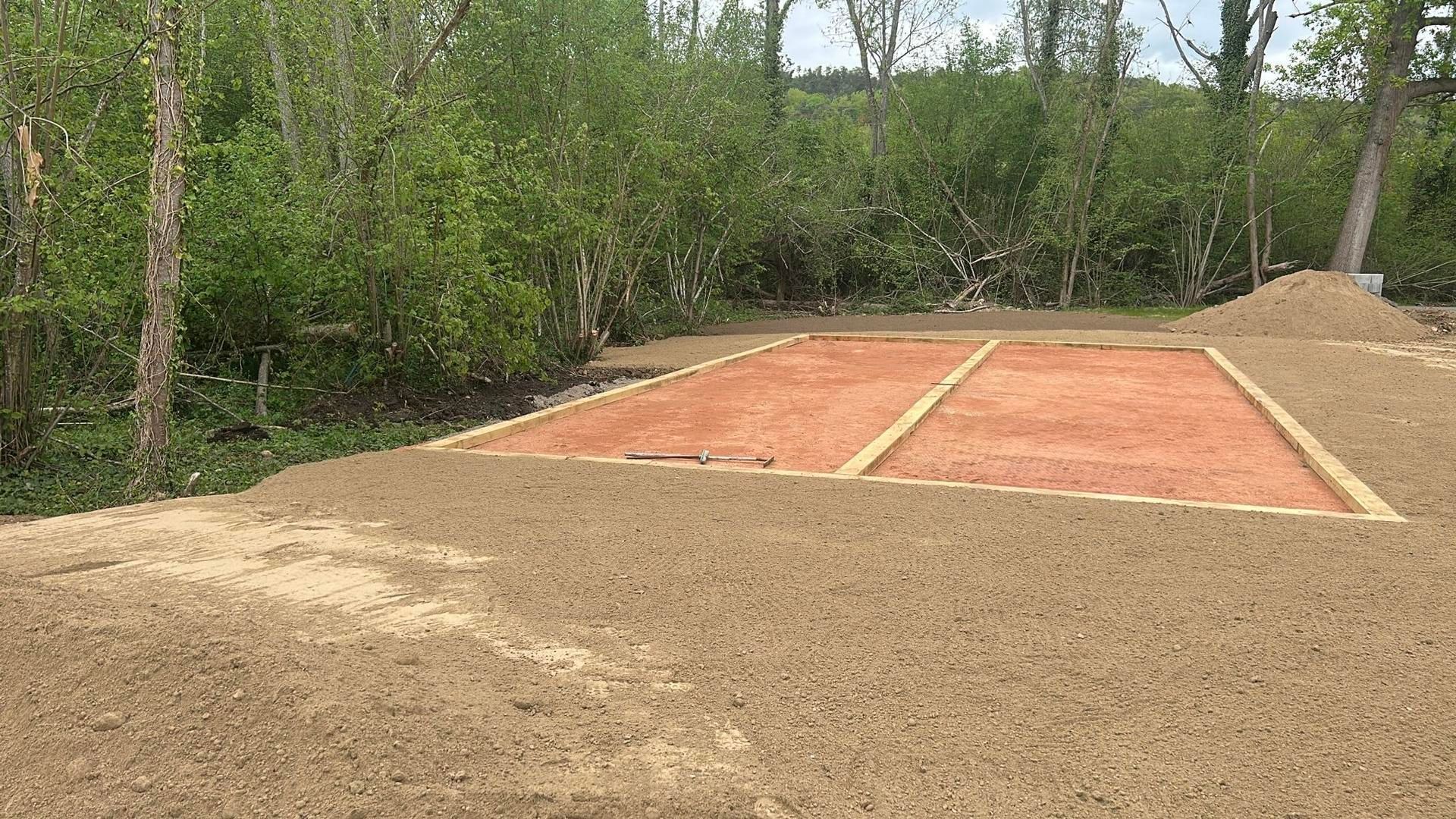Terrain de sable extérieur avec cadre en bois près d'une zone boisée.