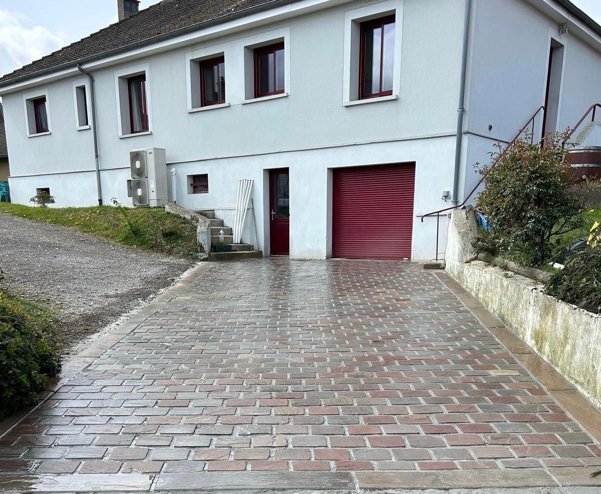 Maison blanche avec allée en briques et porte de garage rouge dans une rue résidentielle en pente