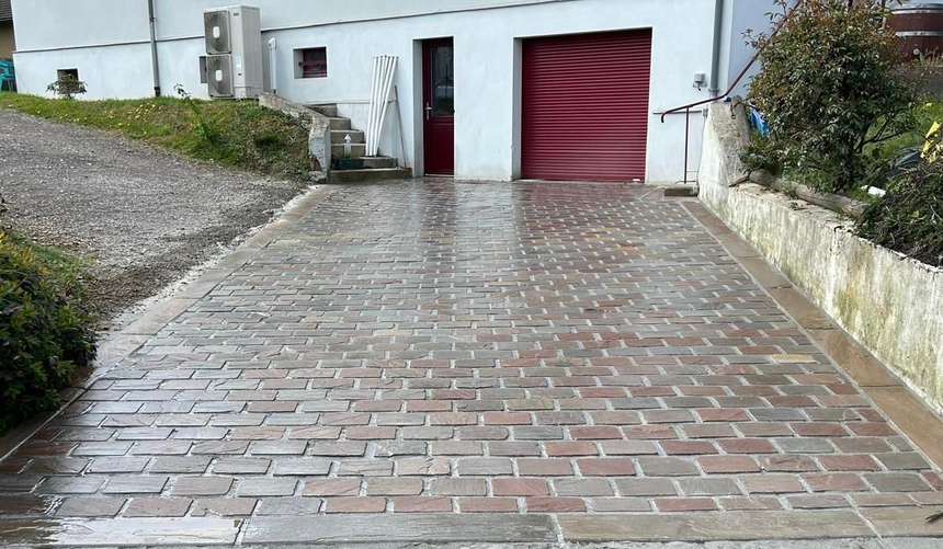 Maison blanche avec allée en briques et porte de garage rouge dans une rue résidentielle en pente.