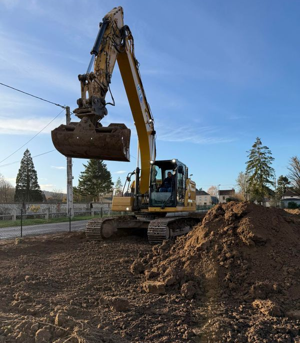 Une pelleteuse jaune déplace de la terre sur un chantier de construction à côté d'une maison.