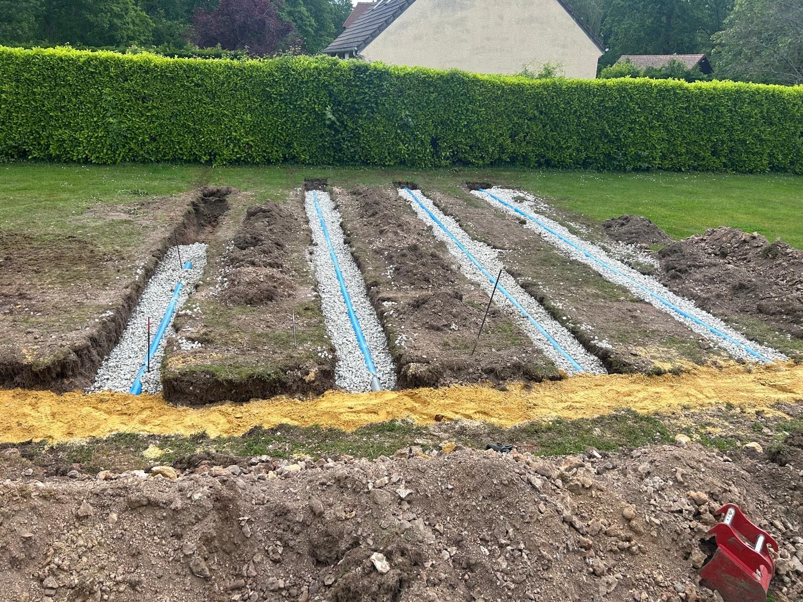 Massif de jardin composé de quatre longues rangées recouvertes de paillis plastique bleu et blanc, bordé de gazon et de haies.