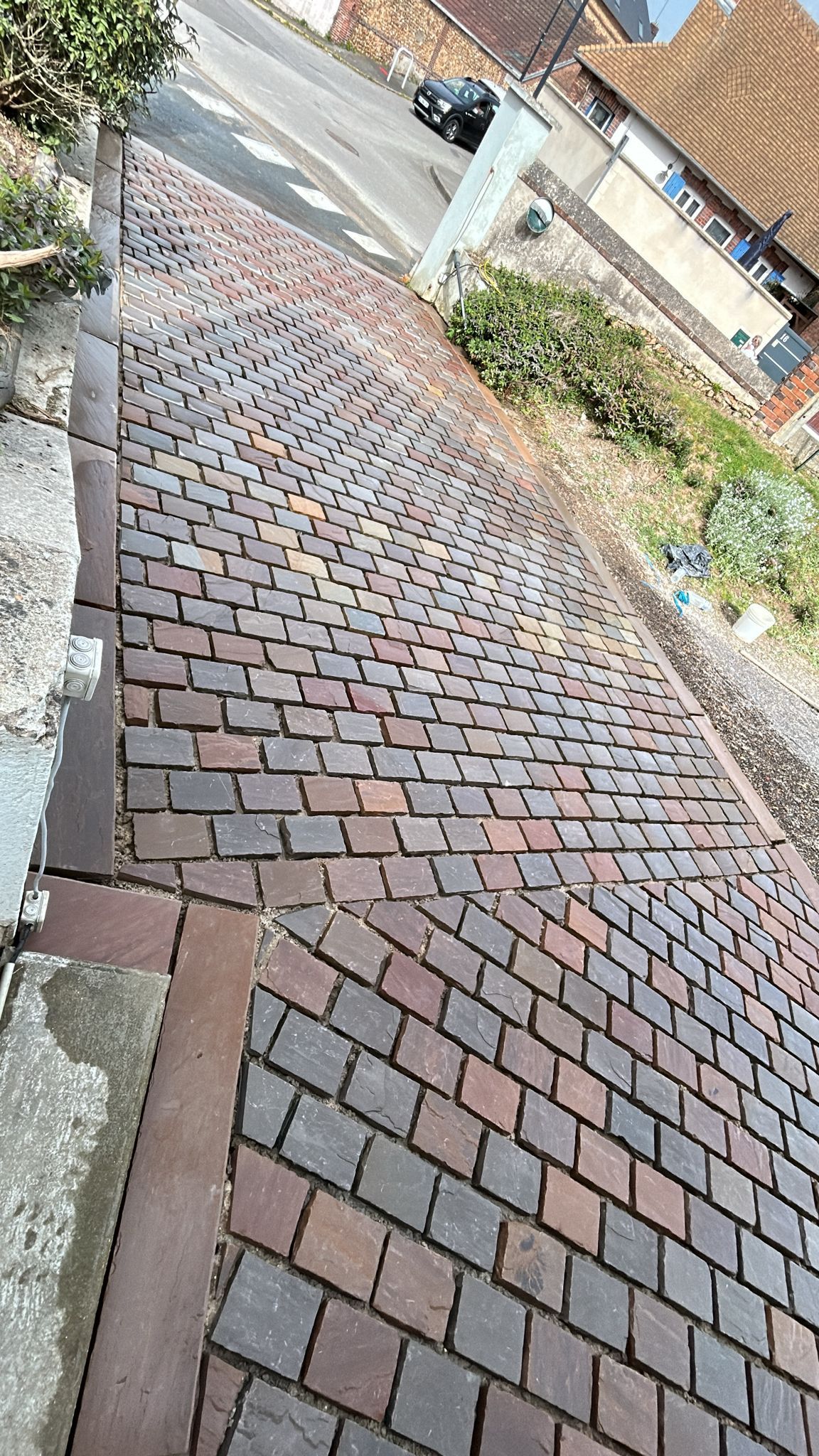 Trottoir en briques escarpé avec une rambarde métallique, vu d'en haut sur une rue en pente.