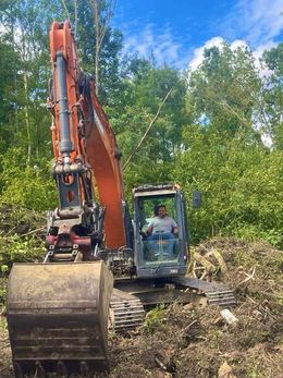 Une pelleteuse jaune déplace de la terre devant une maison en construction