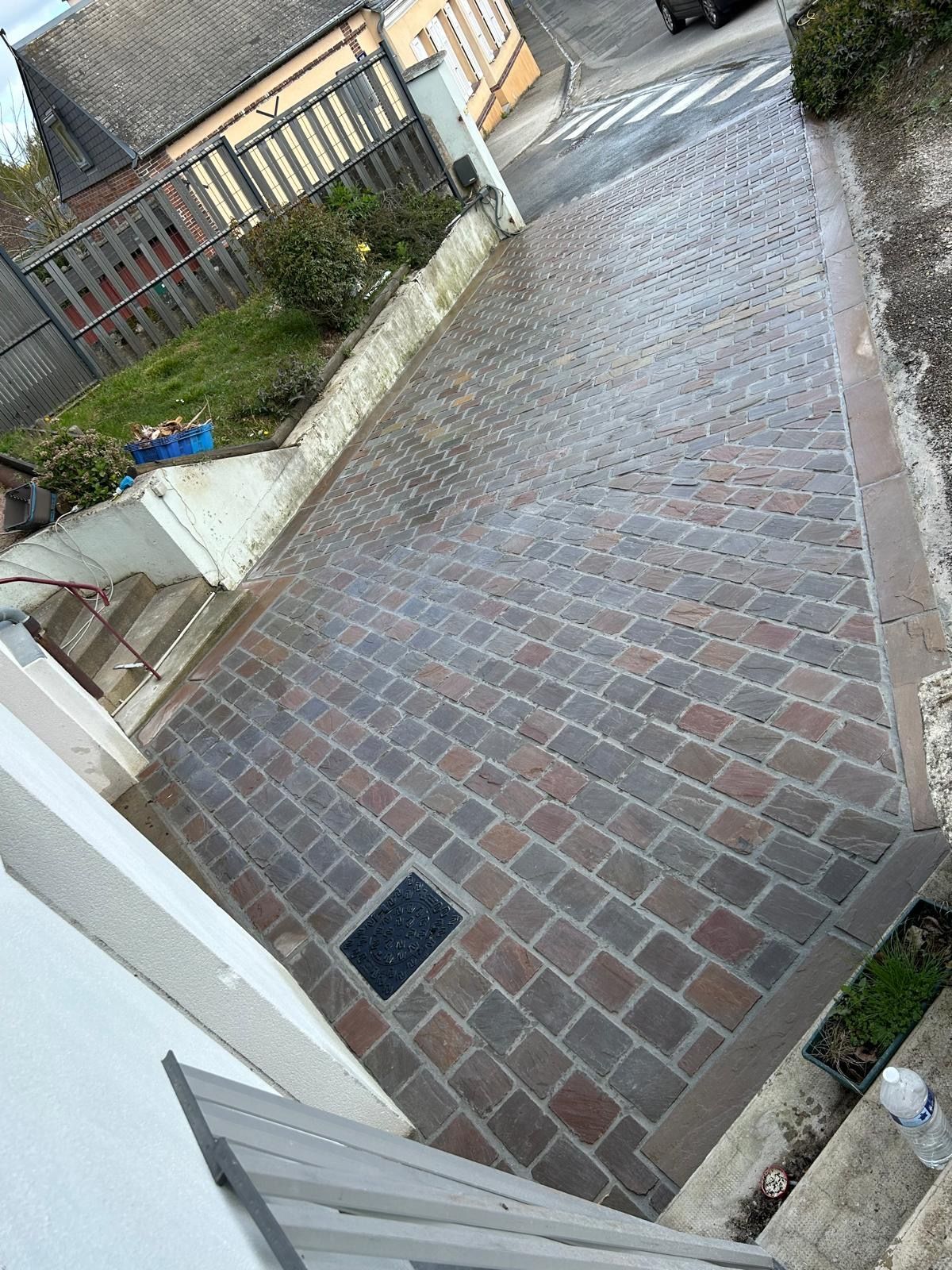 Allée pavée longeant une maison et un jardin, avec des marches et une voiture garée au loin.