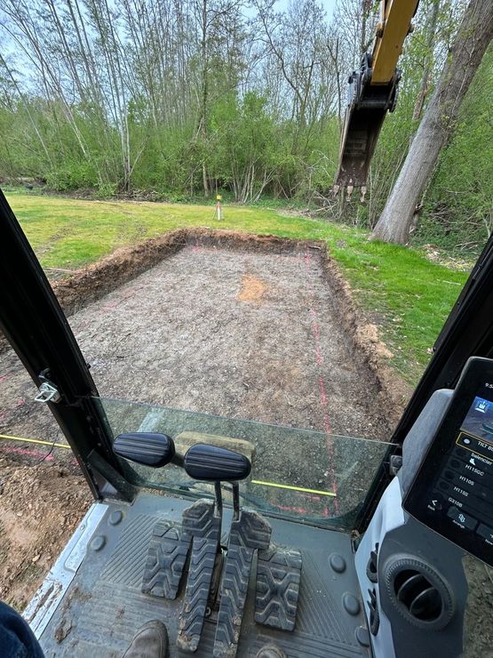 Tranchée avec un tuyau bleu posé dans du gravier entre des monticules de terre, vue d'en haut avec un tracteur au loin.