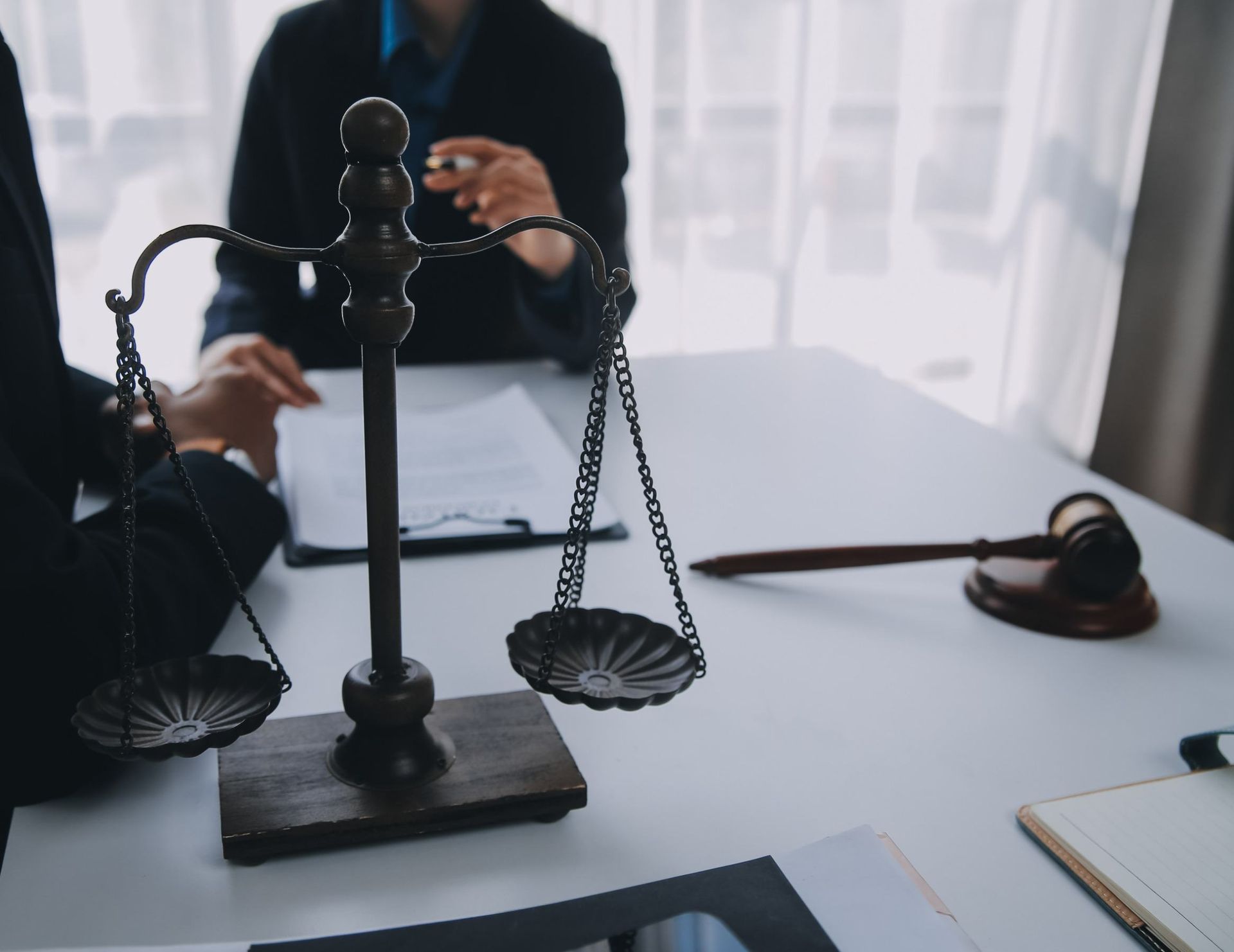 Dos abogados están sentados en una mesa con una balanza de justicia y un mazo.