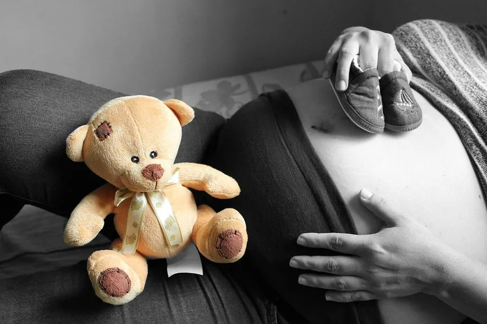 Ventre d'une maman enceinte avec ourson en peluche et chaussons de bébé