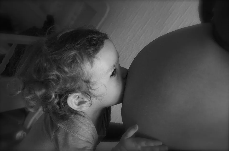Petite fille faisant un bisou sur le ventre de sa maman enceinte