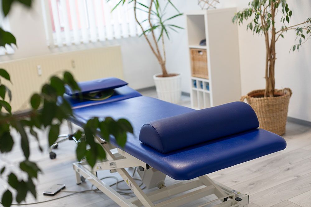 Eine blaue Massageliege in einem Raum mit einer Pflanze.