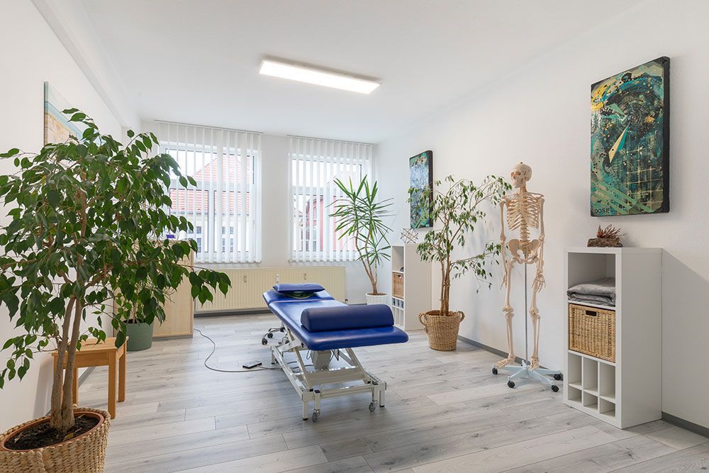 Ein Raum mit einem blauen Tisch, einem Skelett, Pflanzen und einem Gemälde an der Wand.