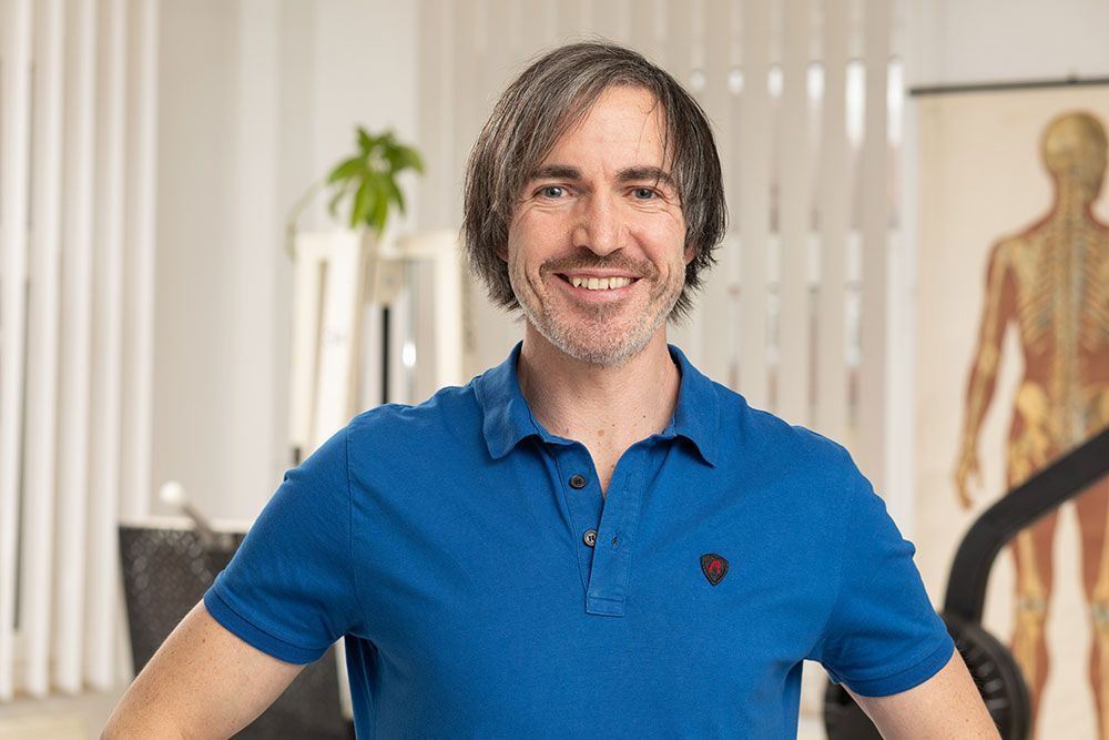 Ein Mann in einem blauen Poloshirt lächelt vor einem Modell eines menschlichen Körpers.