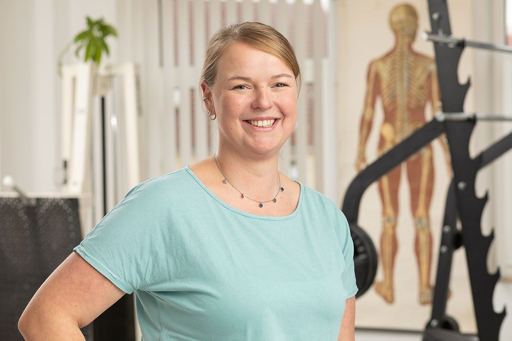 Eine Frau in einem blauen Hemd steht vor einem Fitnessgerät und lächelt.