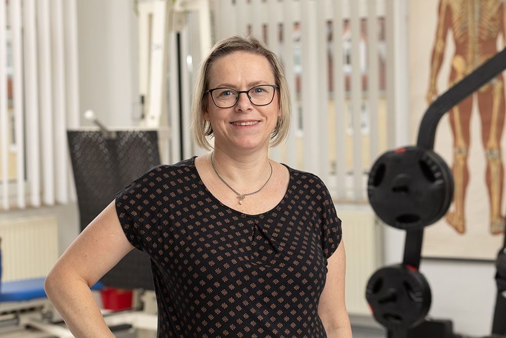Eine Frau mit Brille und schwarzem Shirt steht in einem Fitnessstudio.