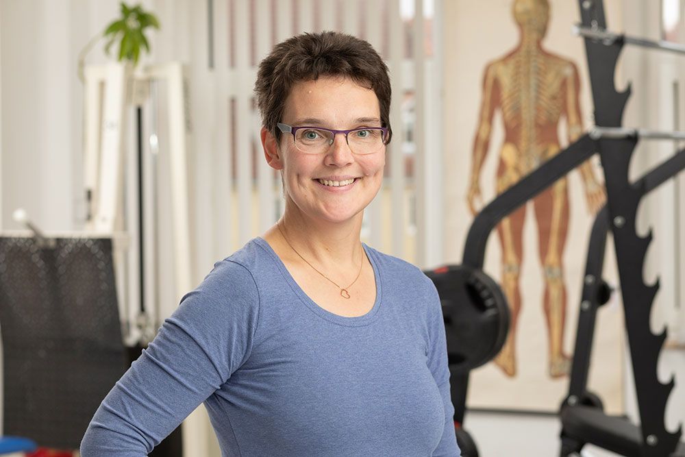 Eine Frau mit Brille und blauem Hemd steht in einem Fitnessstudio.