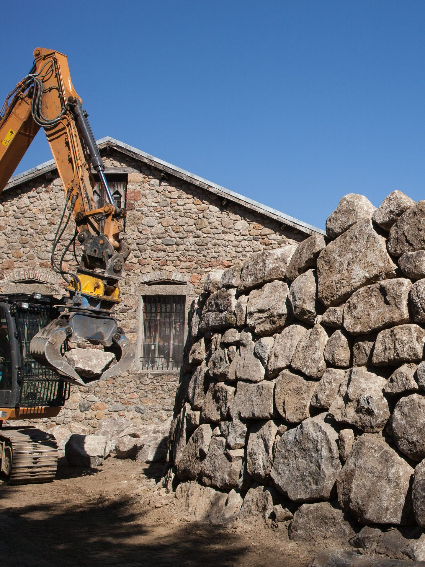 Une pelleteuse dépaçant un rocher devant un mur d'enrochement