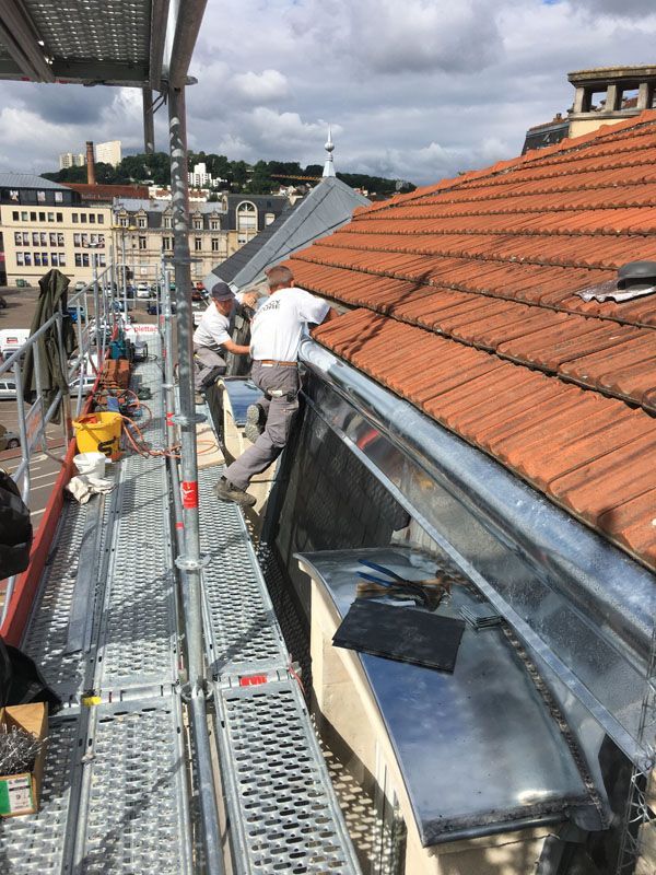 Deux ouvriers qui installent une zinguerie sous une toiture en tuiles